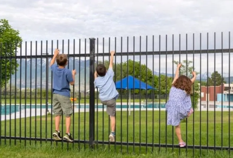 Children looking through a black aluminium pool fence at a swimming pool