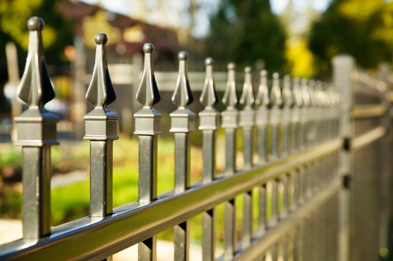 A close-up photograph of a black metal picket fence with pointed finials