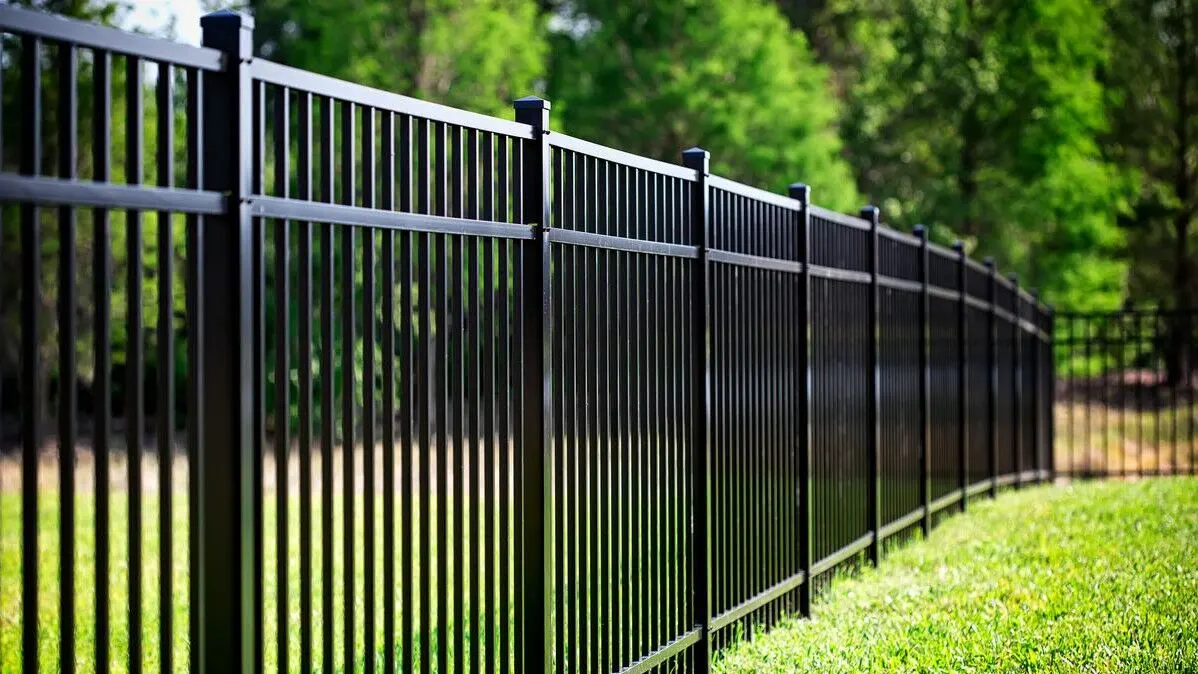 A black metal fence installed along a grassy lawn