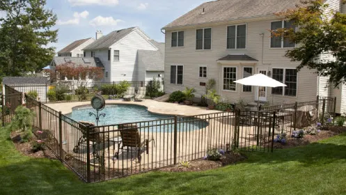 Black metal pool fence enclosing a backyard swimming pool beside a family home