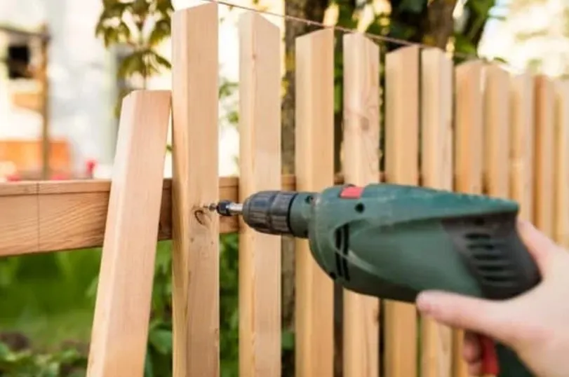 Builder using a cordless drill to fix timber palings to a fence rail