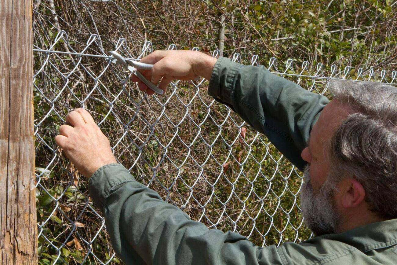 A man using pliers to install a chain link fence