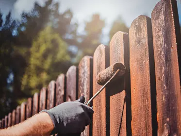 A person painting a wooden fence with a roller