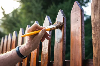A person painting a wooden fence with a brush