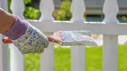A hand painting a wooden fence with a brush