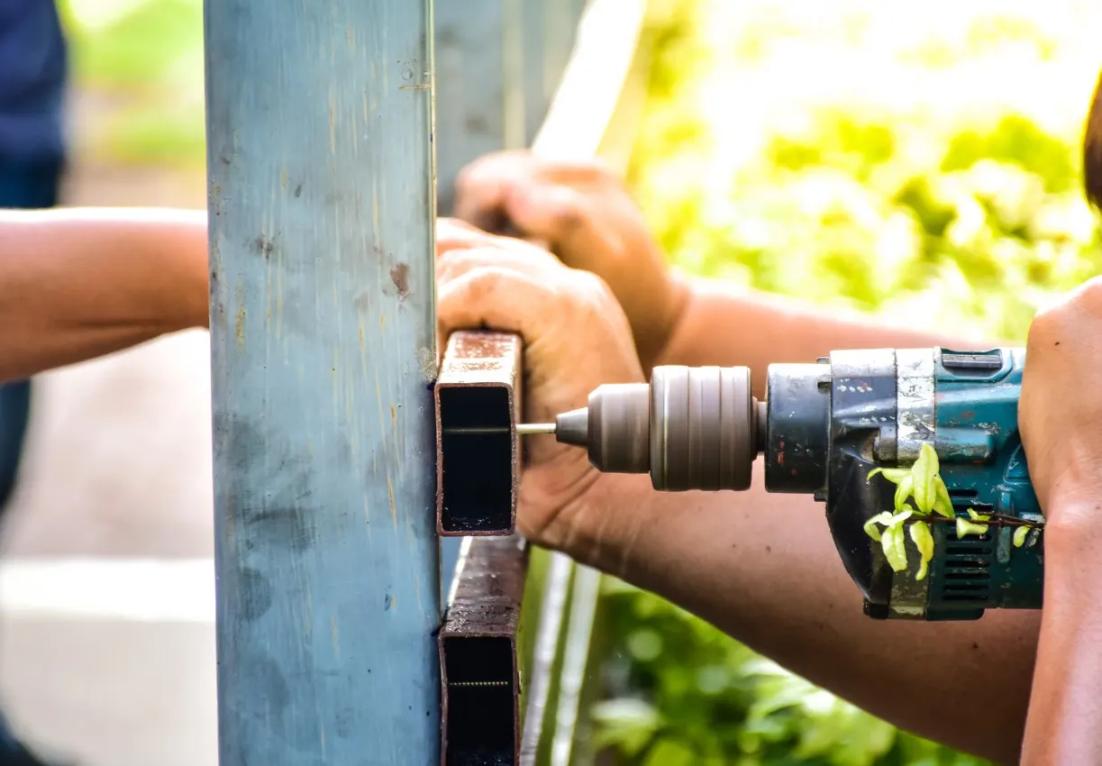 Fencing contractor drilling a rail into a metal post while repairing a damaged fence