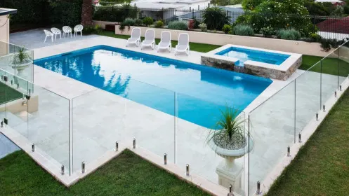 A glass pool fence surrounding a swimming pool in a backyard