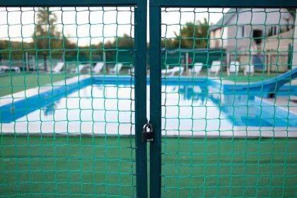 A green chain link fence gate in front of a swimming pool