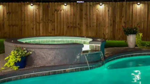 Pool and spa lit at night with downlights along a timber privacy fence