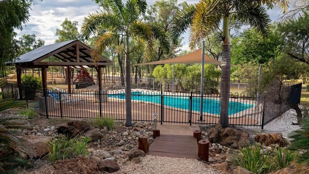Black metal pool fence enclosing a backyard swimming pool with palm trees and a shade sail