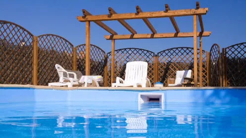 A swimming pool with a wooden pergola and lattice fencing in the background