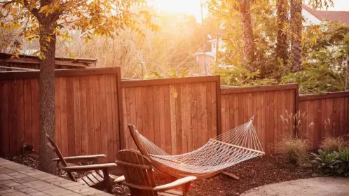 A wooden fence in a backyard with a hammock and trees