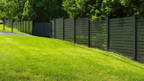 Black horizontal slat fence following the contour of a grassy slope