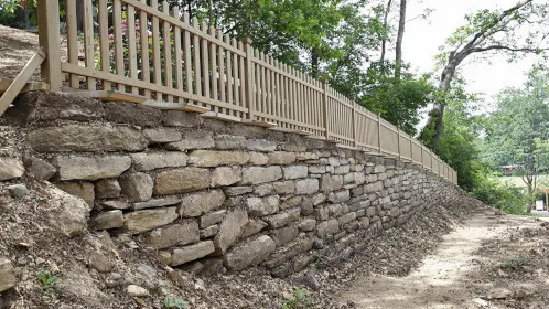A wooden fence installed atop a stone retaining wall on a sloped property