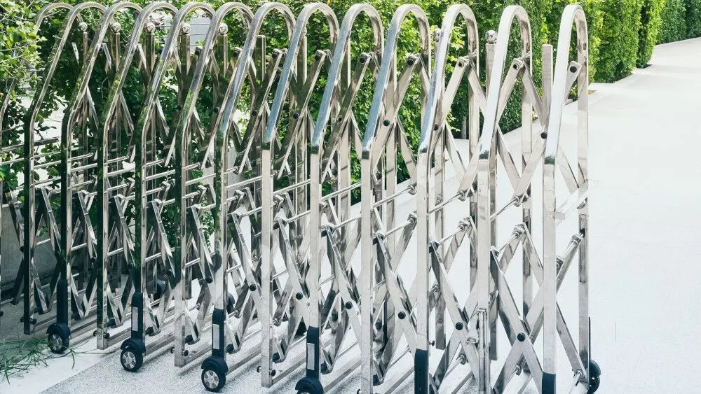 Portable expandable steel temporary fencing panels on wheels beside a hedge