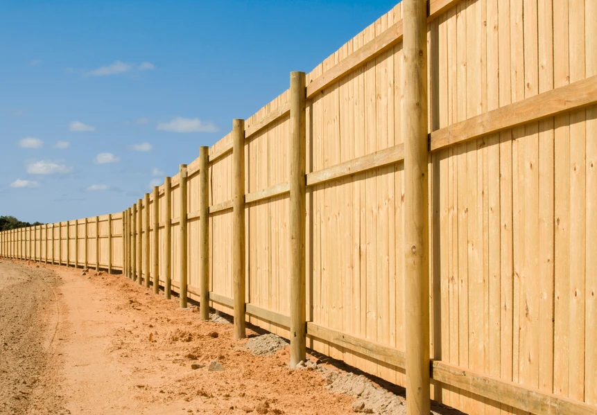 A tall timber paling fence with round posts stretching along a property boundary