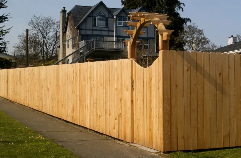 A wooden privacy fence with an arched gate in front of a house