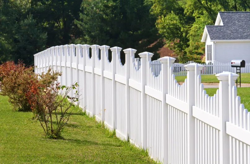 White vinyl picket fence surrounding a green lawn with a house in the background