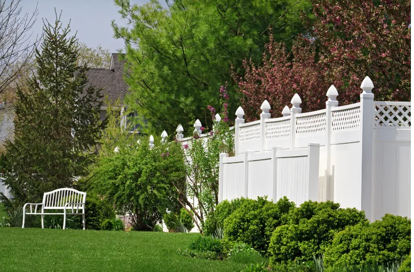 White vinyl privacy fence with lattice top running along a landscaped garden with a lawn and bench