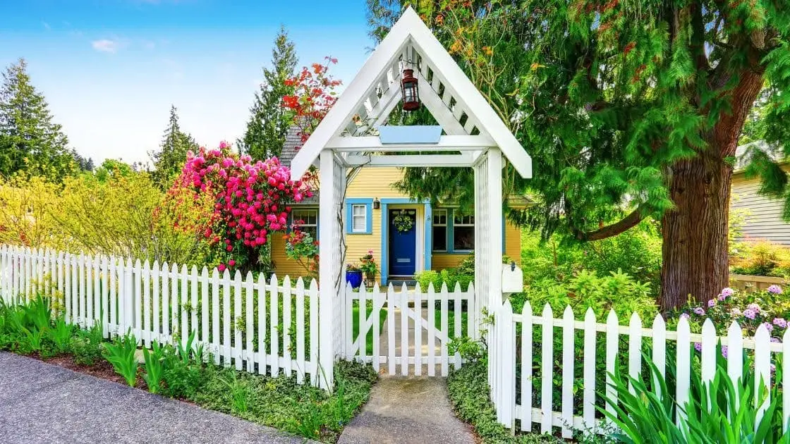 White timber picket fence and arched gate in front of a cottage garden