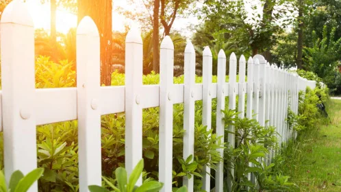 White picket fence bordering a lush green garden at sunset