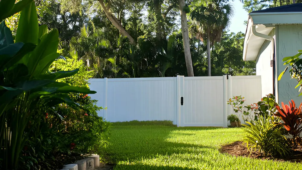 A white privacy fence installed in a backyard with green grass and trees