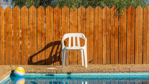 A white plastic chair sits in front of a wooden fence next to a swimming pool